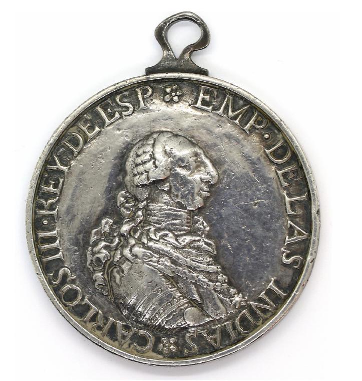 Silver Indian Peace Medal of King Carlos III of Spain, showing a right-facing profile bust of the monarch in armor with a powdered wig. Inscription around the edge reads “CARLOS III REY DE ESP EMP DE LAS INDIAS.