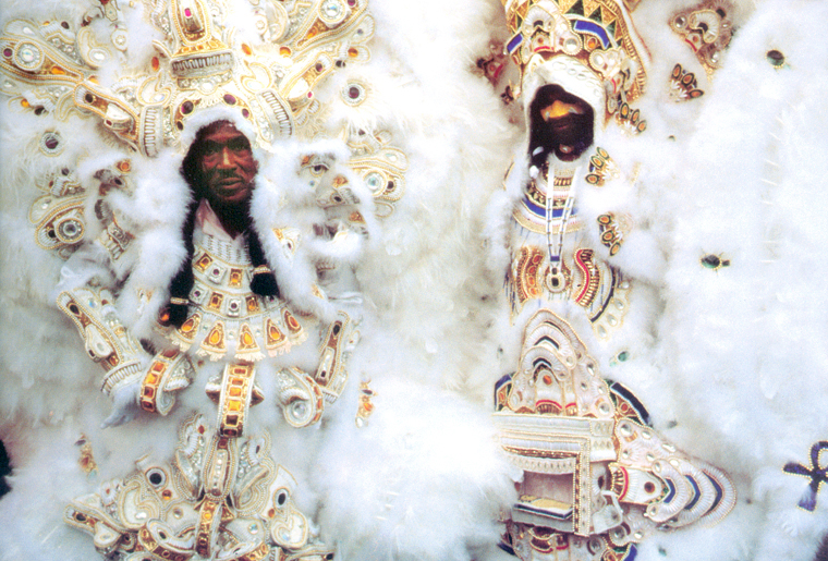 Two Mardi Gras Indians wearing elaborate white, gold, and beaded suits stand side by side, featuring intricate featherwork and detailed chest pieces from their 1997 regalia.
