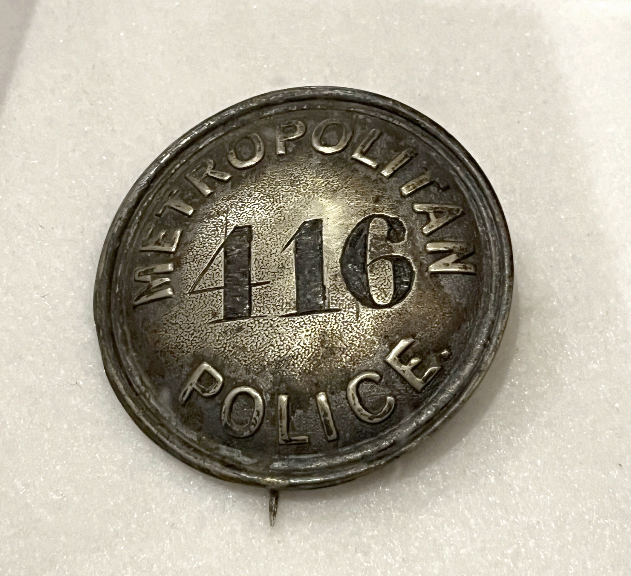 Close-up of a dark metal Metropolitan Police badge or button with the number “416” in the center and the words “Metropolitan Police” raised around the edge.