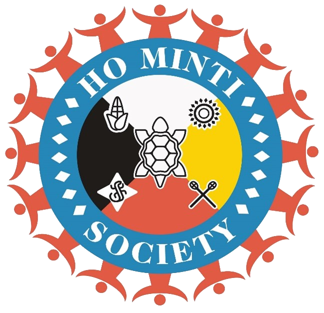 Circular logo for the Ho Minti Society. A blue ring with white text surrounds a central emblem divided into black, yellow, and red sections. In the center is a turtle icon, with additional symbols including corn, a sun, crossed sticks, and a geometric motif. Stylized red human figures form a radiating border around the outer edge.
