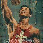 Poster for the documentary The Ragin’ 13. The image shows a victorious weightlifter in a red singlet featuring a large white fleur-de-lis, holding a trophy high overhead. His face is lit with pride and determination. The background is textured in warm tones, with laurels along the bottom noting multiple film festival awards. Text at the top reads “The Ragin’ 13.”