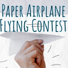 Promotional graphic reading “Paper Airplane Flying Contest” in large blue-outlined text over a light, textured background. A hand in the foreground holds a folded white paper airplane, angled as if about to launch, with simple line accents suggesting motion.