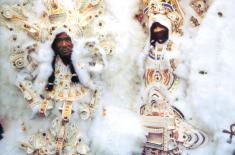 Two Mardi Gras Indians wearing elaborate white, gold, and beaded suits stand side by side, featuring intricate featherwork and detailed chest pieces from their 1997 regalia.