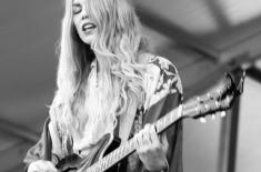 Black-and-white photo of musician Kristin Diable performing onstage, singing while playing an electric guitar.
