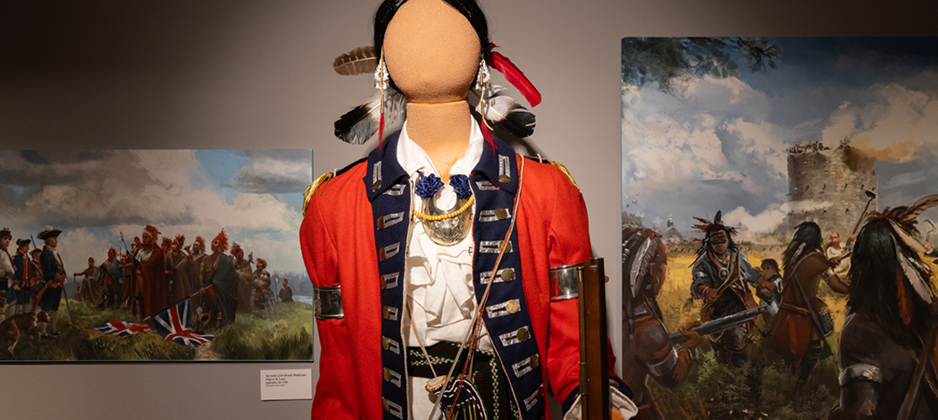 Mannequin dressed in an 18th-century military uniform with a red coat, blue trim, and decorative medals stands centered in a gallery. The figure wears feather adornments and holds a musket. Behind it, two large paintings depict scenes of colonial-era conflict, including soldiers and Indigenous warriors in battle near a fort under a cloudy sky.